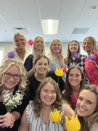 Special education seniors gather with Newton’s adviser, Sara Platt (bottom left), for a celebration before graduation. Submitted photo. The group of 10 women hold up yellow, purple, and pink flowers.