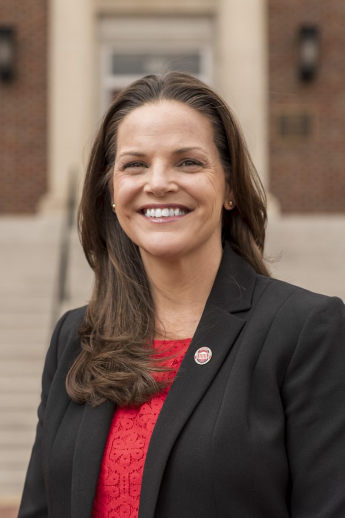 Woman in red blouse, black blazer, and UM lapel pin smiles in front of the Guyton Hall steps.
